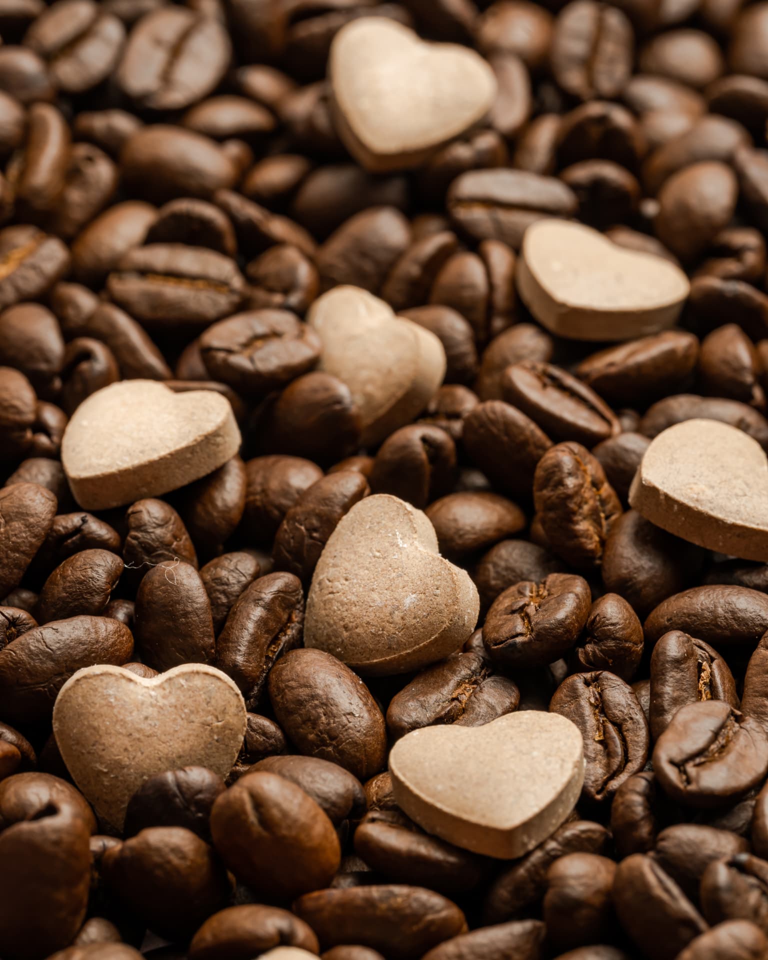 Heart-shaped Coffee & Chitin tablets scattered on roasted coffee beans